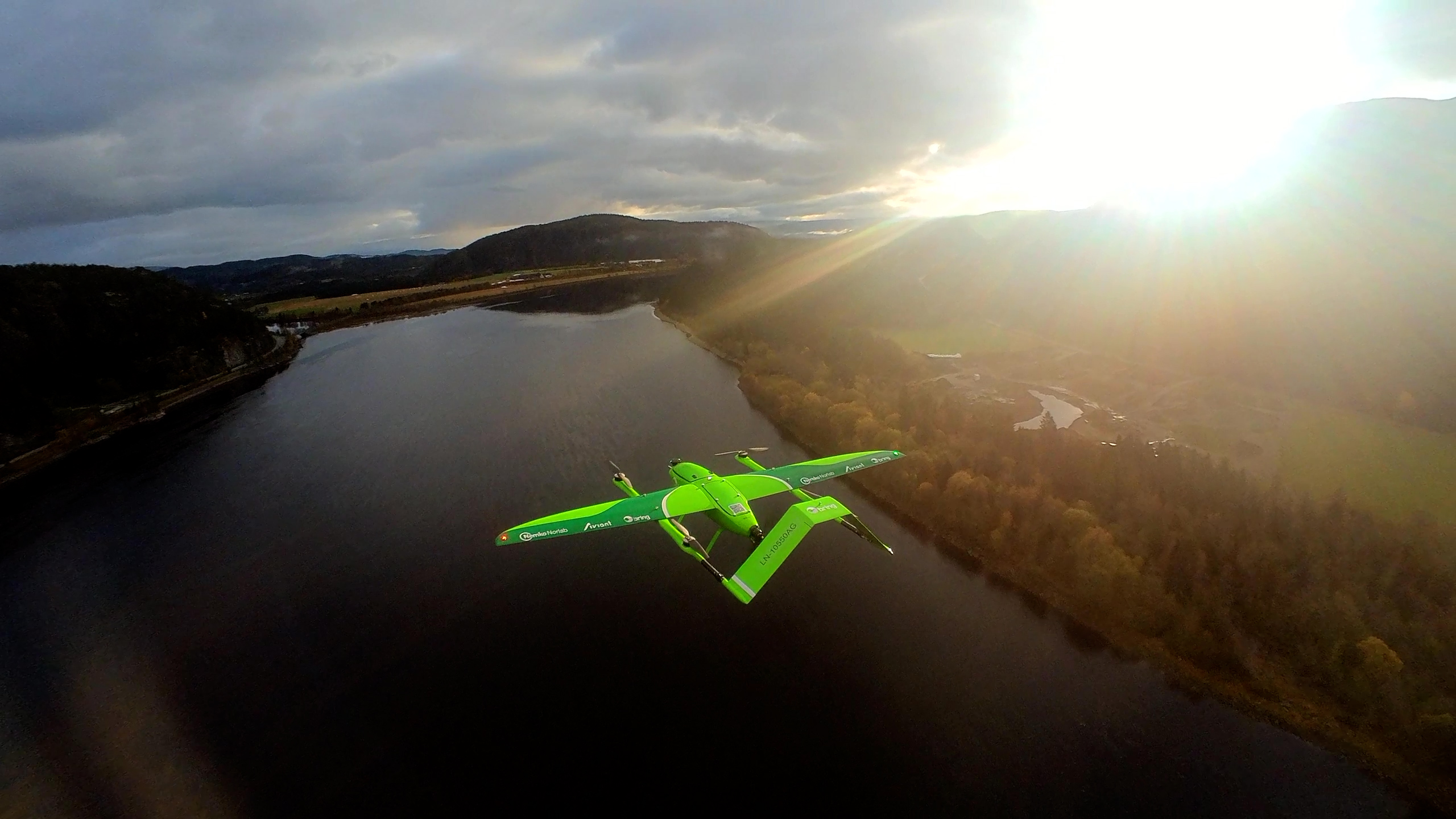 Grønn drone i luften over vann og land